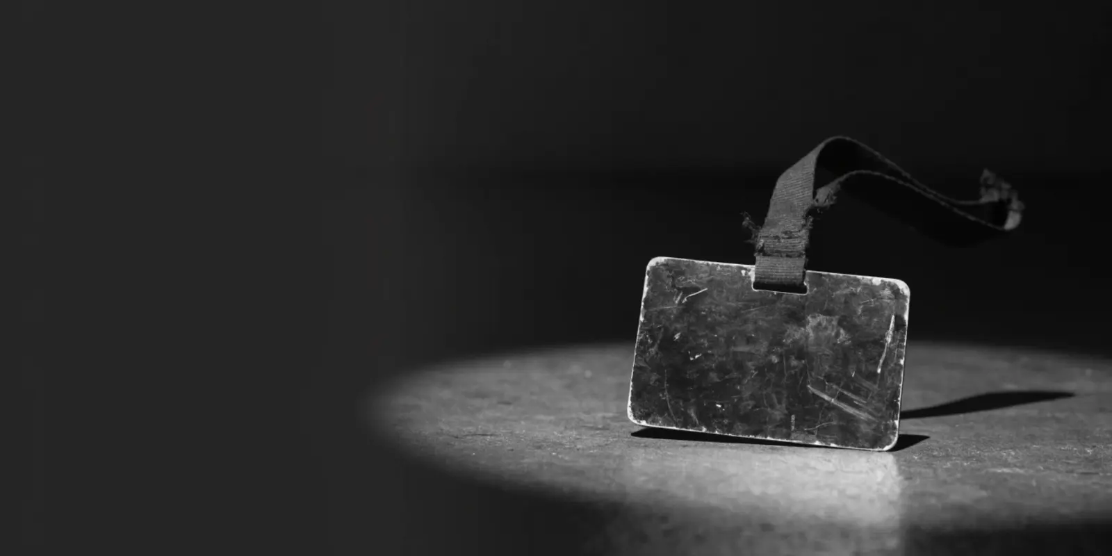 Black and white photo of an old employee badge with a broken lanyard, symbolising data of former employees