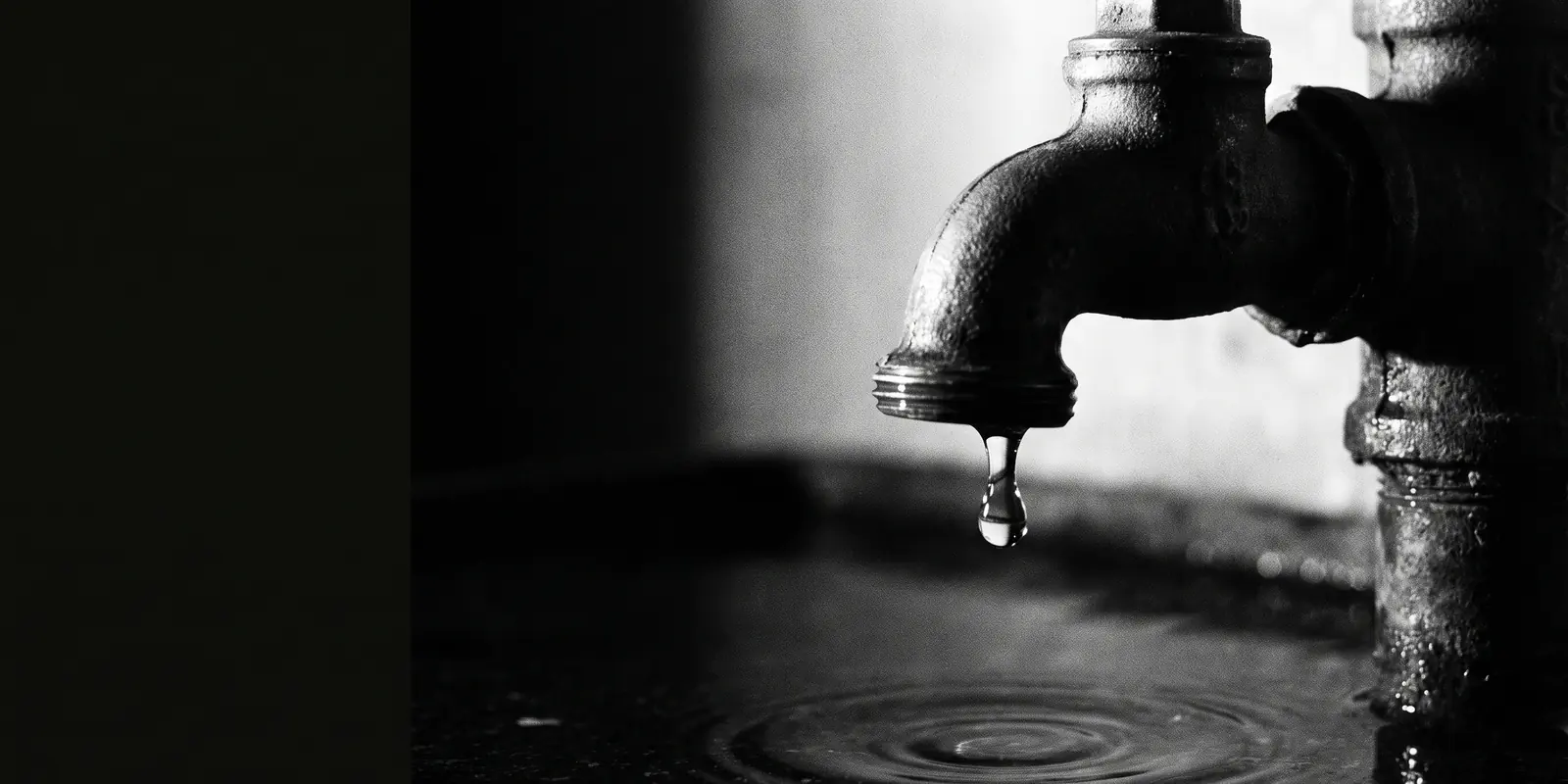 Een druppel valt van een oude kraan in rimpelend water in het donker — beeld voor geld dat ongemerkt uit je ICT wegdruppelt.