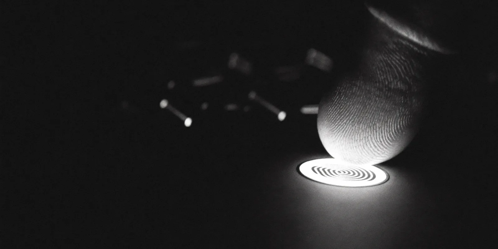 A fingertip touching an illuminated sensor, in black and white against a dark background, as an image for signing in with a passkey instead of an SMS code.